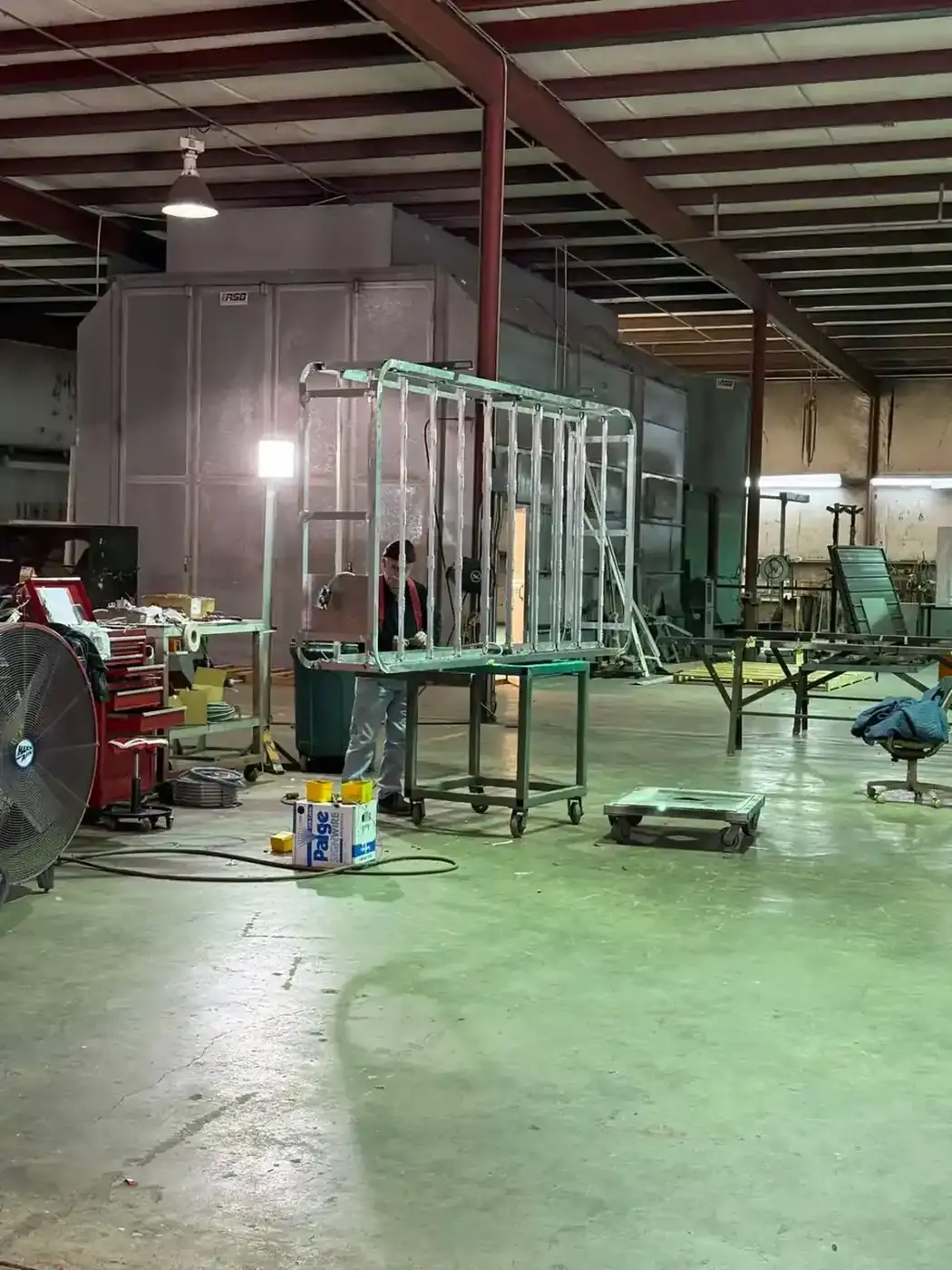 Fabricator welding a large steel sign cabinet frame on a rolling table inside the fabrication shop