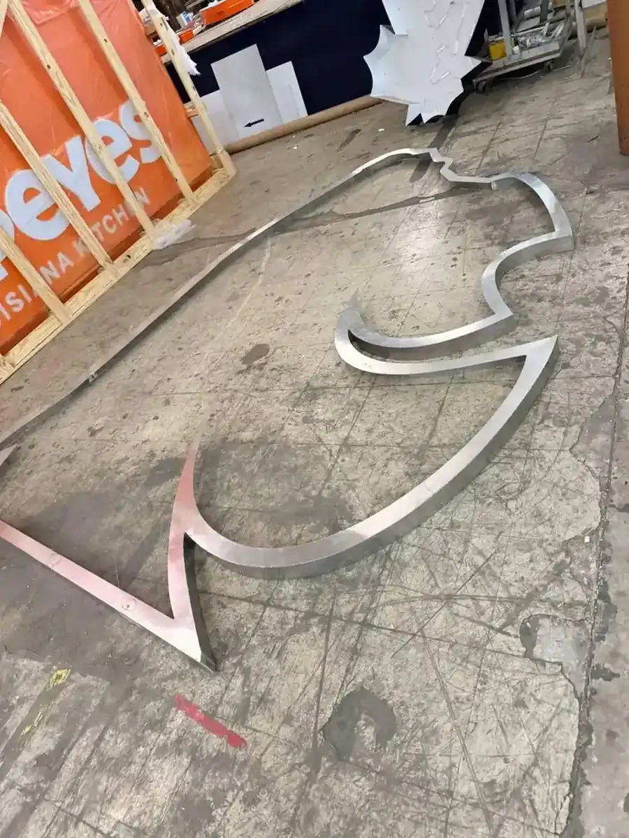 Cut and formed aluminum returns outlining a large sign logo laid out on the shop floor before welding